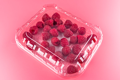 A lot of ripe raspberries in a closed, plastic package on a light pink background.