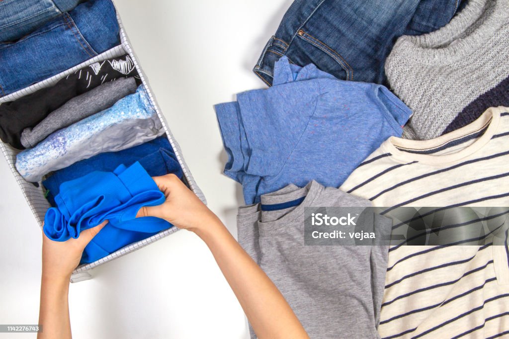 Vertical storage of clothing, tidying up, room cleaning concept. Hands tidying up and sorting kids clothes in basket. Woman hands tidying up kids clothes in basket. Vertical storage of clothing, tidying up, room cleaning concept. Clothing Stock Photo