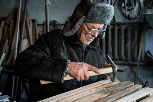 istock Old senior carpenter in grey warm clothes in eyeglasses 1142295387