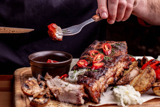 deliciosas costillas asadas sazonadas con una salsa picante y servido con hierbas frescas picadas en un viejo tablero de madera rústica en una cocina campestre. - rubbing spice rib barbecue fotografías e imágenes de stock