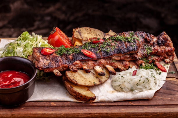 deliciosas costillas asadas condimentadas con hierbas frescas, ensalada de col, patata apoyada en un viejo tablero de madera rústica - rubbing spice rib barbecue fotografías e imágenes de stock