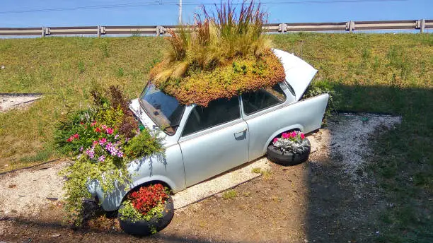 Budapest, Hungary - Aug 8, 2018: Beautiful funny vintage Trabant car parking behind an unknown parking house planted colorful flowers