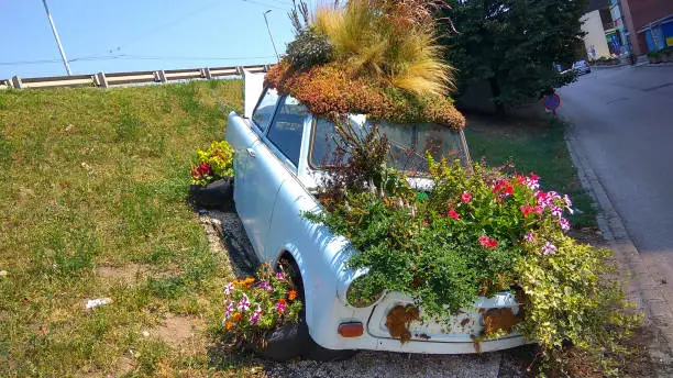 Budapest, Hungary - Aug 8, 2018: Beautiful funny vintage Trabant car parking behind an unknown parking house planted colorful flowers