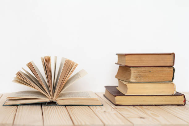 istock An open book next to a stack of vintage books on a wooden surface against a white wall. 1142300714