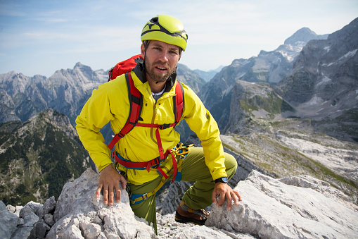 Man with mountain climbing equpment climbing to the top of the mountain range. Hemlet, backpack, shoes. Beautiful mountains in the background.