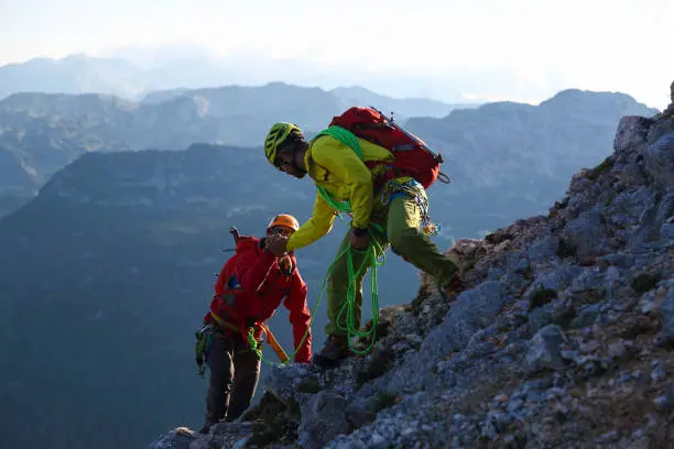 Male mountain climber is helping his friend to the top.