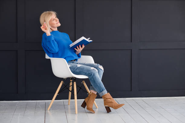 aged female diary inspiration imagination thinking Aged female with diary. Inspiration and imagination. Smiling woman sitting on modern white chair thinking, dreaming. womens blue suede shoes stock pictures, royalty-free photos & images