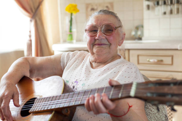 зрелые женские увлечения, 90-летняя бабушка играет на гитаре. пожилая женщина дома. - one person lifestyles 80 plus years indoors стоковые фото и изображения