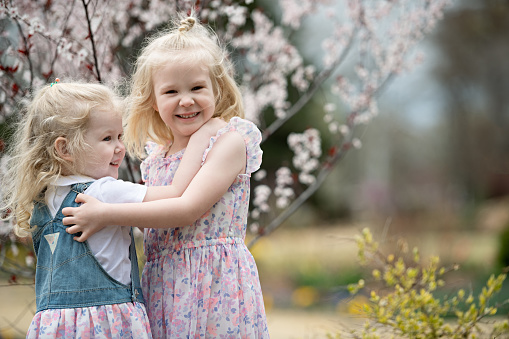 Two blonde girls are hugging in the flowering garden