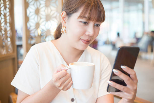 istock Young Beautiful Asian Woman Using Phone and Drinking Coffee 1142348224