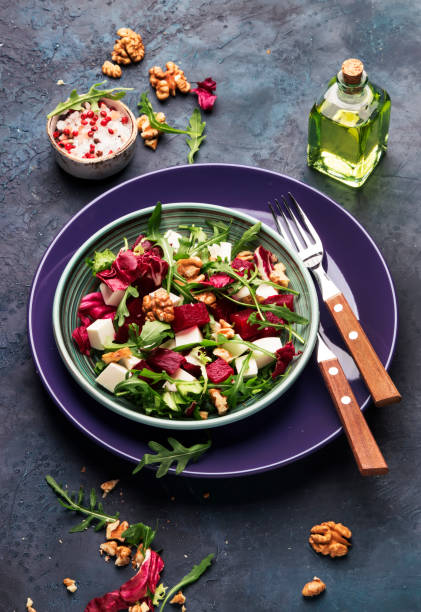 istock Beet or beetroot salad with fresh arugula, radicchio, soft cheese and walnuts on plate with fork, dressing and spices on blue kitchen table, copy space, top view 1142350504