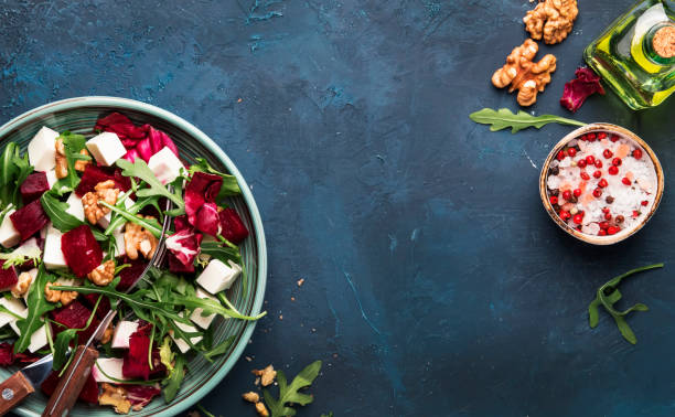 istock Beet or beetroot salad with fresh arugula, radicchio, soft cheese and walnuts on plate with fork, dressing and spices on blue kitchen table, copy space, top view 1142350512