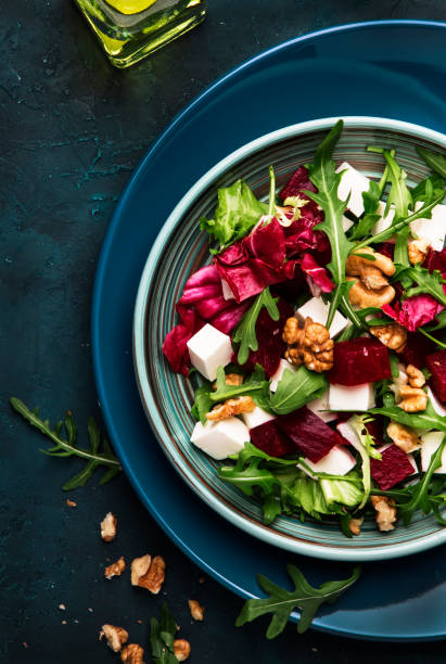 istock Beet or beetroot salad with fresh arugula, radicchio, soft cheese and walnuts on plate with fork, dressing and spices on blue kitchen table, copy space, top view 1142351025