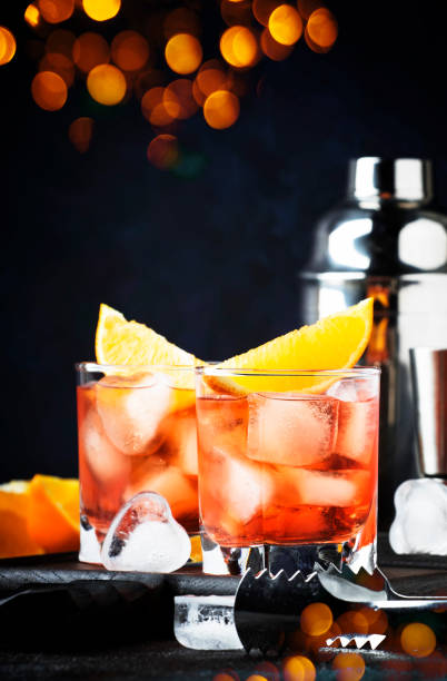 Trendy alcoholic cocktail Negroni with dry gin, red vermouth and red bitter, orange slice and ice cubes. Brown bar counter background, bar tools, night mood, copy space, selective focus cóctel alcohólico de moda negroni con ginebra seca, vermut rojo y rojo amargo, rebanada de naranja y cubitos de hielo. brown barra de fondo del contador, herramientas de barra, estado de ánimo nocturno, espacio de copia, enfoque selectivo