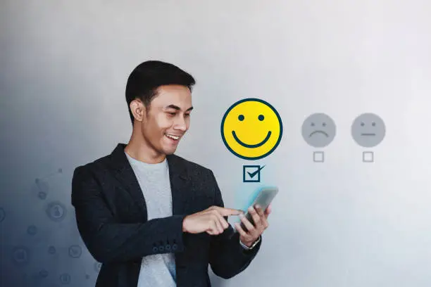 Photo of Customer Experience Concept. Young Businessman Giving his Positive Review in Satisfaction Online Survey. Happy Client Submit a Smiling Face for Excellent Services via Smartphone