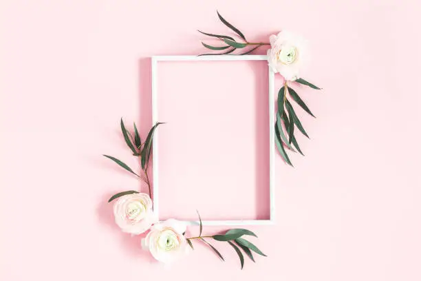 Photo of Flowers composition. White flowers, eucalyptus leaves, photo frame on pastel pink background. Flat lay, top view, copy space