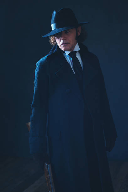 istock Victorian man in long black coat and hat holding rifle. 1142361888