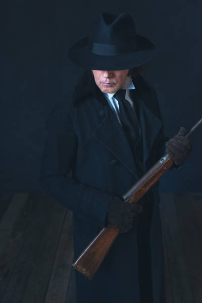istock Victorian man in long black coat and hat holding rifle. 1142361890