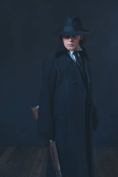 istock Victorian man in long black coat and hat holding rifle. 1142361896