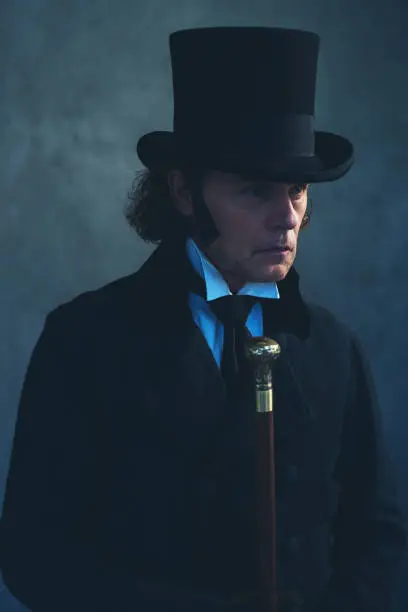 Photo of Edwardian man in long black coat and hat holding cane.