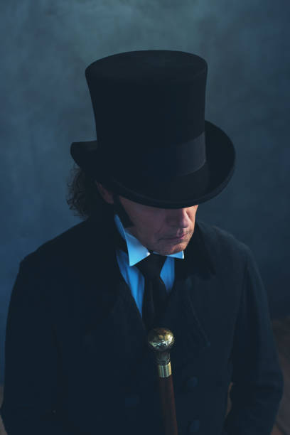 istock Edwardian man in long black coat and hat holding cane. 1142361963