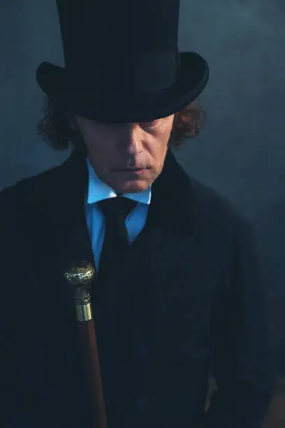 Photo of Edwardian man in long black coat and hat holding cane.