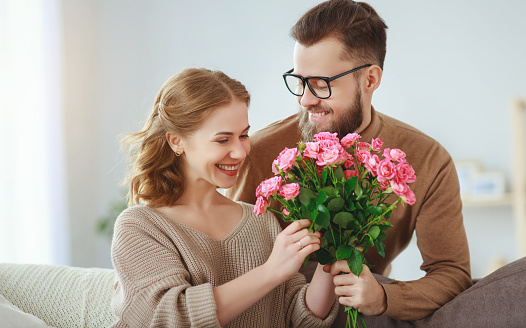 happy loving married couple. husband gives his wife flowers at home