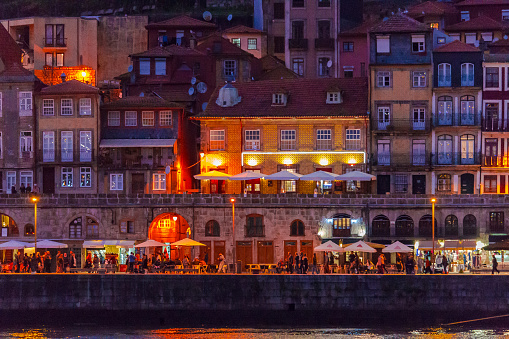 View of old town Porto at night with outdoor cafes and people eating and drinking.  Buildings along the riverside featuring characteristic Portuguese architecture.