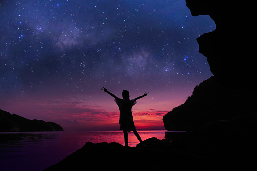 The girl standing on the rocks near the beach with beautiful million stars galaxy