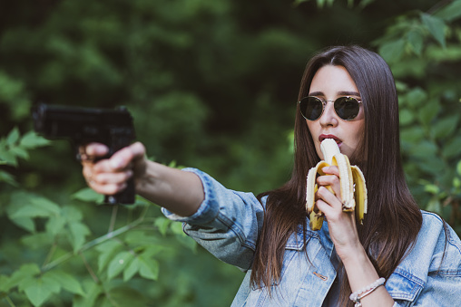 girl eats a banana and at the same time aims from a pistol