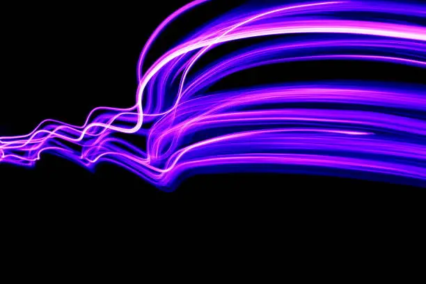 Photo of Long exposure photography, light painting - vibrant intense neon purple color in an abstract wavy pattern, against a black background