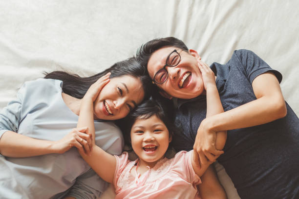 счастливая азиатская семья, лежа на кровати в спальне со счастливым и улыбчивый, вид сверху - азиатского и индийского происхождения стоковые фото и изображения