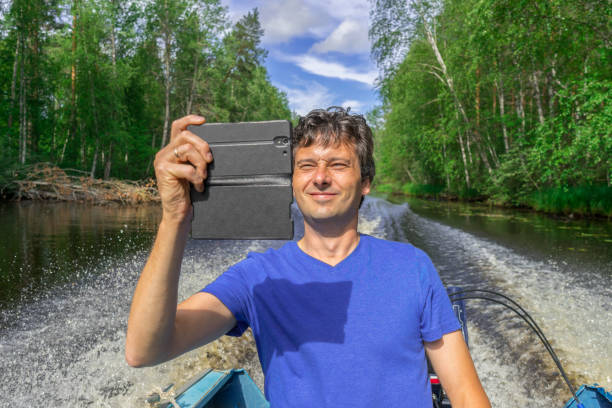 istock Handsome middle-aged man floating on boat along northern river and taking selfie with smartphone on beautiful landscape background in sunny summer day. Travel concept. Chernaya river, Karelia, Russia 1142415305