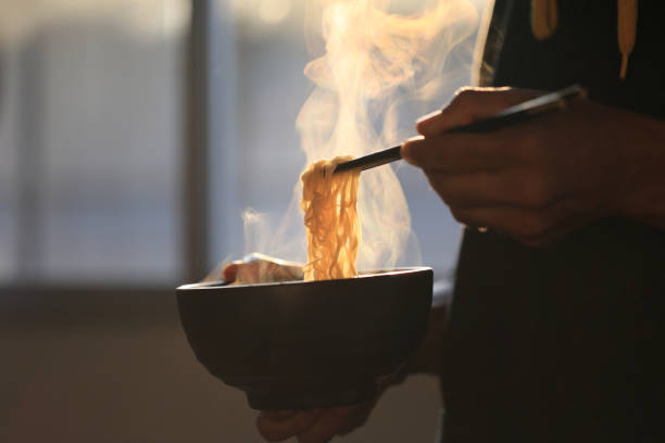 Man hand holding chopsticks of instant noodles in wood bowl with smoke rising in the home, Sodium diet high risk kidney failure, Healthy eating concept Man hand holding chopsticks of instant noodles in wood bowl with smoke rising in the home, Sodium diet high risk kidney failure, Healthy eating concept instant food stock pictures, royalty-free photos & images