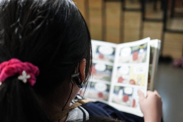 小さな女の子が図書館で読書をしています。補聴器で。 - bookstore student chinese ethnicity book ストックフォトと画像
