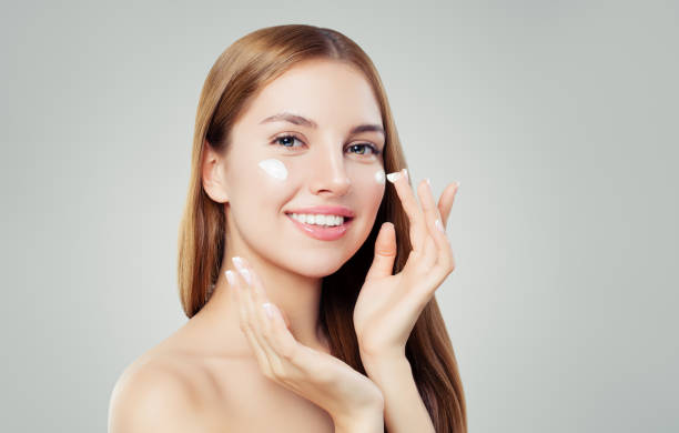 giovane donna felice che applica la crema sul viso. concetto di cura della pelle, bellezza e trattamento del viso - mettersi la crema foto e immagini stock