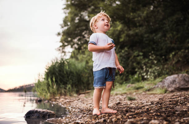 istock A wet, small toddler boy standing outdoors by a river in summer, playing. 1142419818