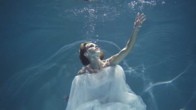 Girl with long hair in a white dress floating underwater