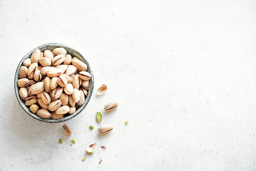 Pistachio nuts. Green salted pistachios in ceramic bowl on white background, copy space, top view.