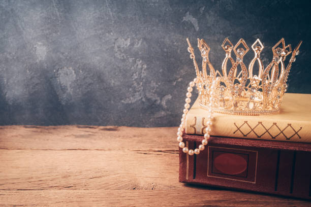 istock Fairy tale crown and old books on wooden table over black background. 1142431599