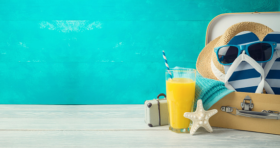 Summer concept background with cute funny flip flops, suitcase and orange juice on wooden table
