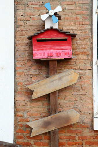 Red wooden letterbox under the small wind turbine on the brick wall. The mailbox with a slot into which mail is placed from the postman.