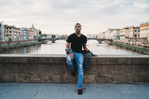 Young adult man portrait in the city during sunset against Arno River, Florence