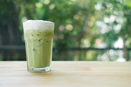 Iced green tea with milk froth on top in glass with ice on table in coffee shop