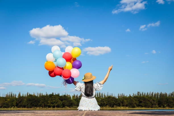 joven hermosa asiática mano sosteniendo globos coloridos sentados en el lago y el cielo azul en el fondo - lake asia young women beautiful people fotografías e imágenes de stock