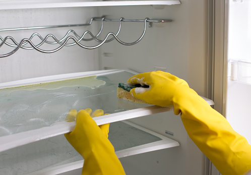 Close up of female hands with protective gloves cleaning empty refrigerator