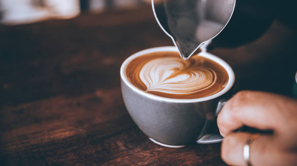 コーヒーラテのアートパターンのハート形で注ぐストリームミルクを作るバリスタ。 - barista coffee coffee crop heart shape ストックフォトと画像
