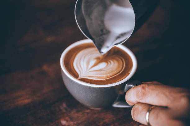 コーヒーラテのアートパターンのハート形で注ぐストリームミルクを作るバリスタ。 - barista coffee coffee crop heart shape ストックフォトと画像