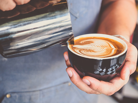 Professional Barista with coffee cup making beautiful latte art pattern.