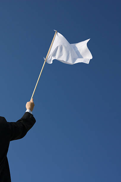 Surrender – Waving the white flag Businessman holding a white flag flutters in the wind against a blue sky. depression behavior businessman economic depression stock pictures, royalty-free photos & images